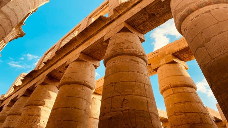 Upward view of towering columns in Karnak Temple, detailed with hieroglyphics against a clear blue sky