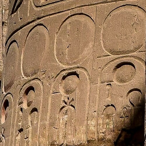 An ancient Egyptian statue with missing upper body parts stands between two walls covered with hieroglyphs in Luxor, Egypt