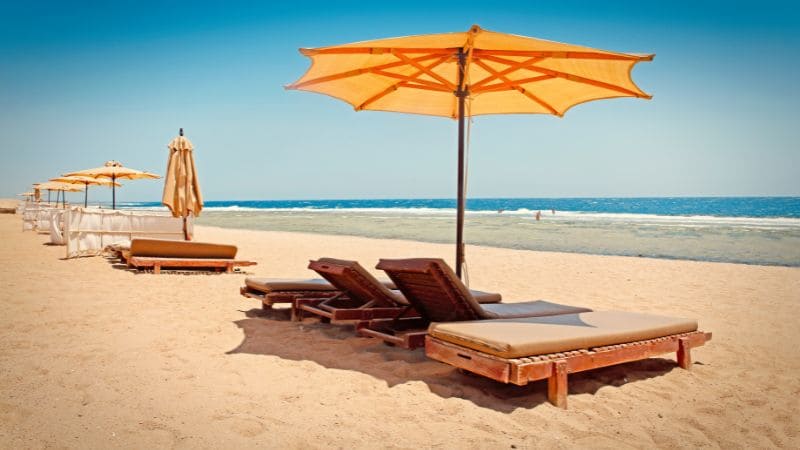Beach loungers under orange umbrellas on a sandy beach with a clear blue ocean.